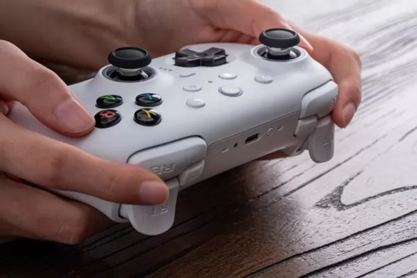 Uma foto de uma pessoa segurando um controlador de jogo branco em uma mesa de madeira